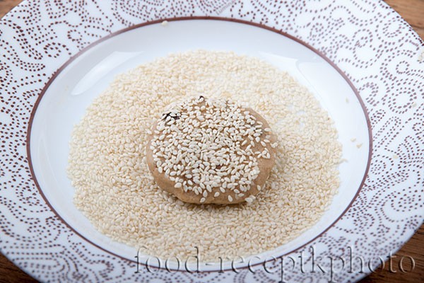 Заготовки для печенья в виде шариков в тарелке с семенами кунжута