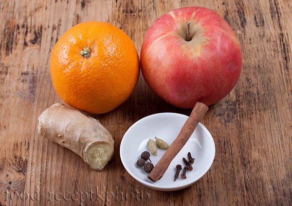 На фото на старом деревянном столе ингредиенты для фруктового пряного чая апельсин,яблоко,корень имбиря и специи