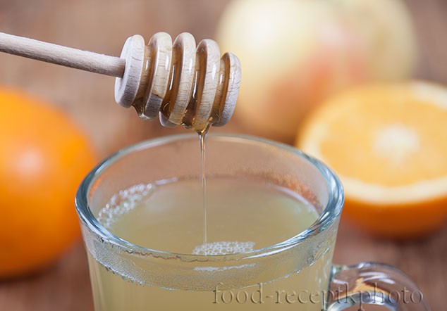 На фото пряный фруктовый чай в чашке для глинтвейна с ложечкой для меда с которой стекает мед