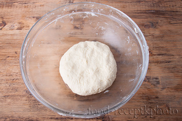 На фото тесто для лукового пирога в стеклянном салатнике на деревянном коричневом столе