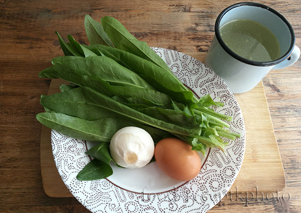 На фото ингредиенты для супа из щавеля:щавель,лук,яйцо и бульон в кружке