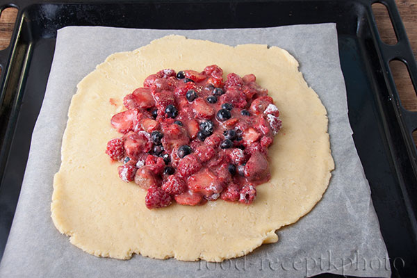 На фото раскатанное песочное тесто с ягодной начинкой для галеты на листе для выпечки на противне
