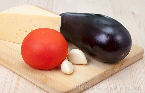 Ингредиенты для запеченных баклажан: помидор,чеснок,сыр,баклажан на разделочной доске
